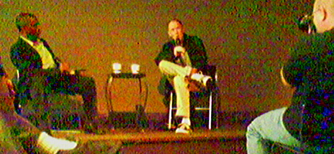 For the stage interview, author and interviewer sat in simple, stackable 
 chairs on a small, raised platform at the front of a large conference room.  Paper take-out cups from Bridgehead sat on a small
 table between them.